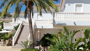 Un complexe hôtelier doté d’un palmier, de chaises longues et d’un escalier menant à un balcon.