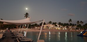 A beachside resort with a pool, lounge chairs, and palm trees.