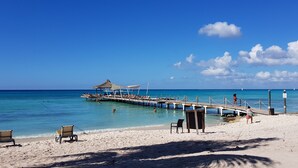 A beach with a pier, lounge chairs, and a thatched-roof structure. - Appartamento vista mare (Bayahibe)