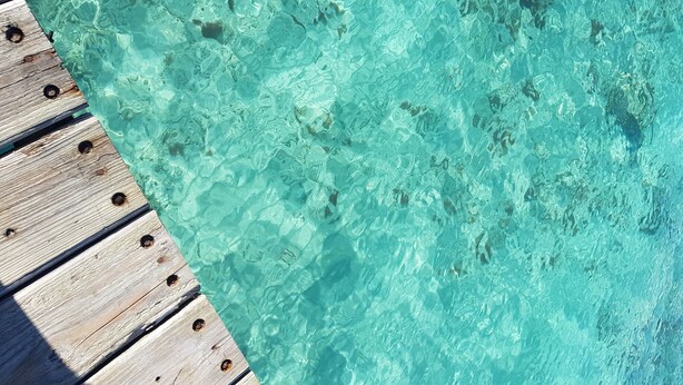 A wooden deck adjacent to a clear turquoise pool. - Appartamento vista mare (Bayahibe)