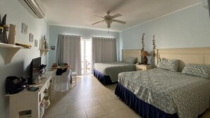 A hotel room with two beds, a ceiling fan, a desk with a chair, and a window with curtains. - Appartamento vista mare (Bayahibe)