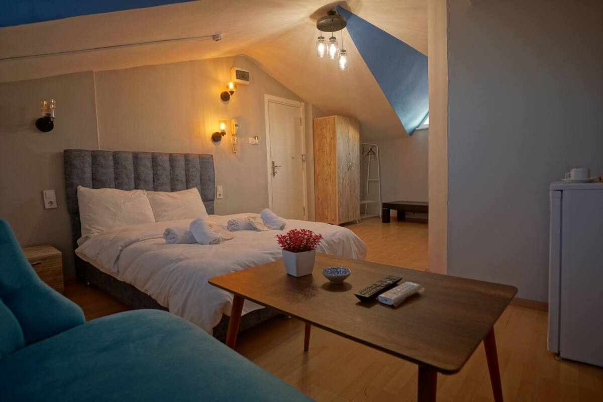 A bedroom with a bed, a wooden wardrobe, a small table with a bowl and remote, and a blue chair.