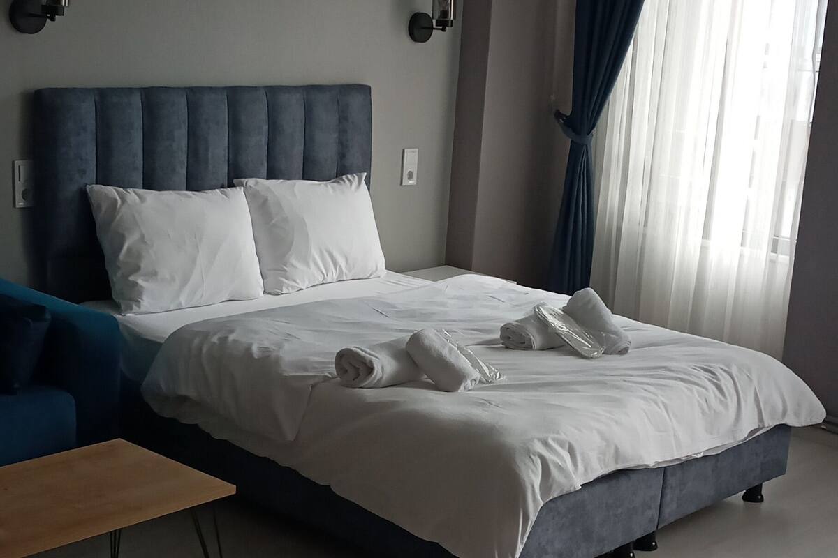 A modern bedroom with a large bed, a wooden nightstand, and a ceiling light fixture.