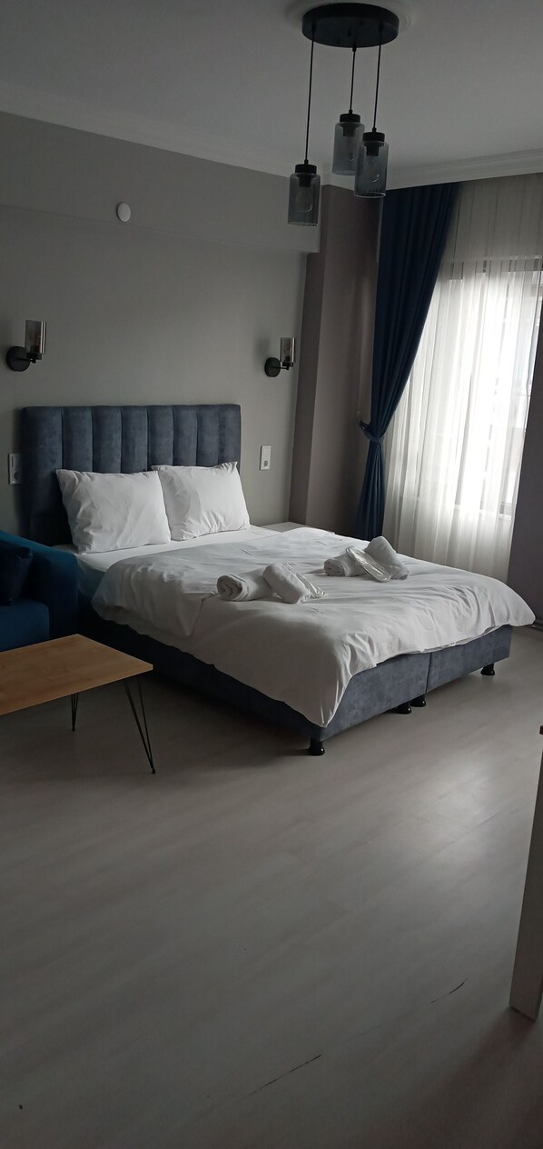 A modern bedroom with a large bed, a wooden nightstand, and a ceiling light fixture.