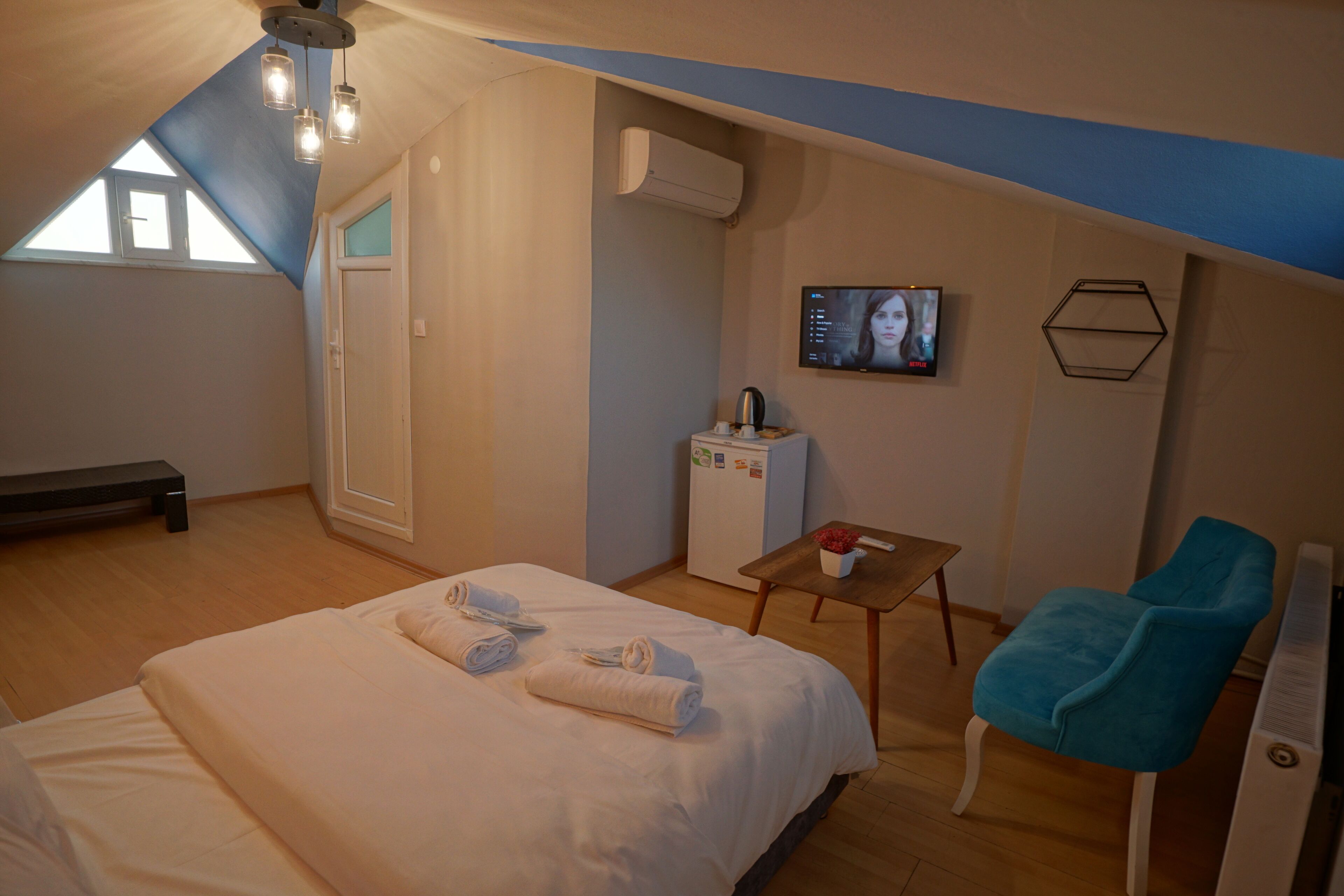 A bedroom with a bed, a bench, a desk with a chair, an air conditioner, and a television.