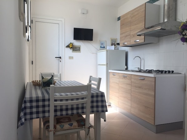 A compact kitchen with a dining area, featuring a checkered tablecloth, wooden chairs, a built-in stove, and a TV mounted on the wall.
