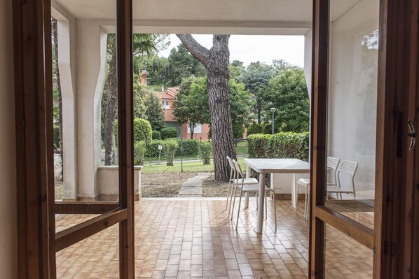 An open patio with a tiled floor, a table with chairs, and a view of a tree and buildings in the background.