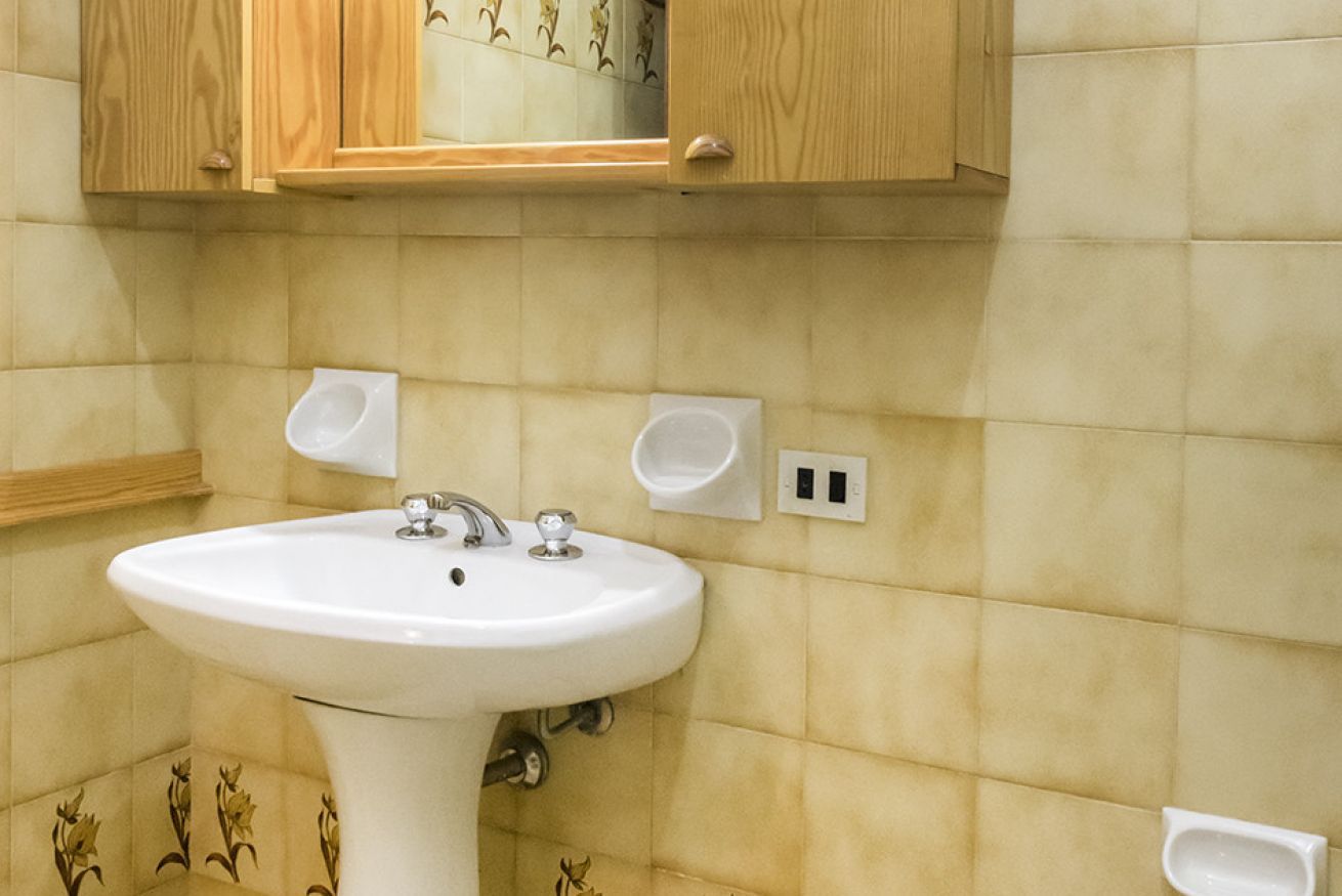 Een badkamer met een wastafel op een voetstuk, houten kastjes en een spiegel.