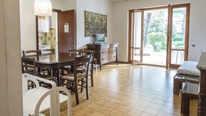 Un coin repas avec une table et des chaises en bois, un téléviseur posé sur un meuble en bois, et une grande fenêtre donnant sur un paysage verdoyant.