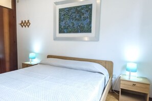 A neatly made bed with a white comforter, two bedside lamps, a framed artwork on the wall, and a wooden nightstand with a drawer.