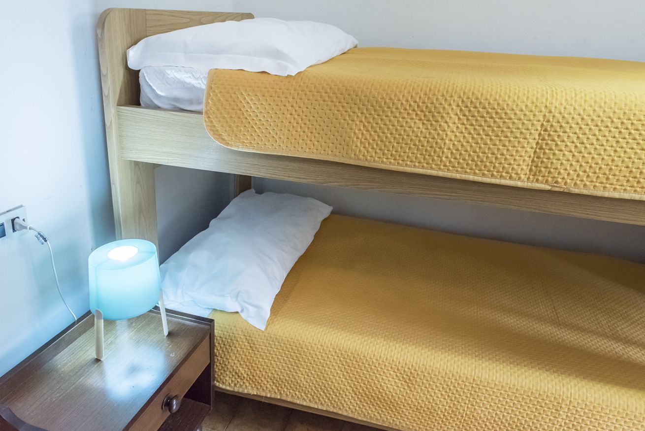 A bunk bed with a yellow mattress, white pillows, and a bedside table with a lamp.