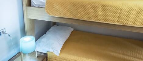A bunk bed with a yellow mattress, white pillows, and a bedside table with a lamp.