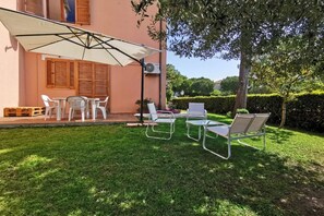 A patio with outdoor furniture, a white umbrella, and a building with wooden shutters.