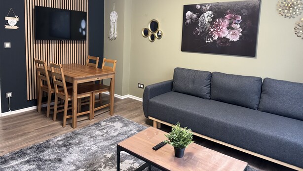 Een moderne woonkamer met een houten eettafel, een grijze bank en een groot bloemenportret aan de muur.