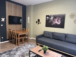 A modern living room with a wooden dining table, grey sofa, and a large floral painting on the wall. - BERLIN PURE - holiday apartment for up to 12 people (Bezirk Neukölln)