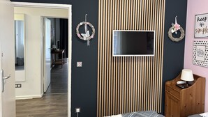Een moderne slaapkamer met een televisie aan een donkere muur, houten lamellen en twee decoratieve kransen.