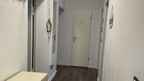 Een gang met een houten vloer, een beige kast met lades en een witte deur met een klein bordje.