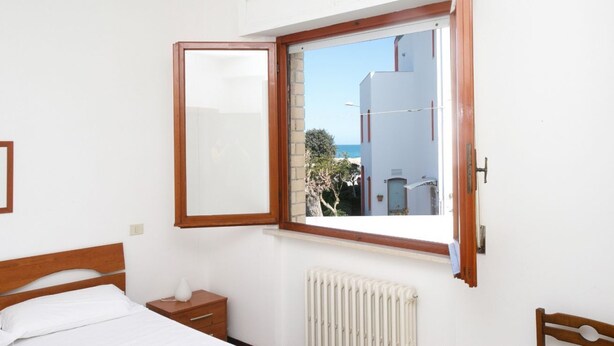Une chambre à coucher avec un lit, une table de chevet, une fenêtre donnant sur des immeubles et des arbres, et un radiateur.