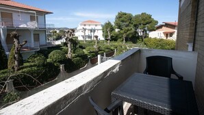 Un balcon avec une table et des chaises, donnant sur un jardin où les arbustes et les arbres sont soigneusement taillés.