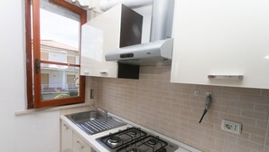 Une cuisine compacte équipée d’une cuisinière à gaz, d’un évier et d’une fenêtre donnant sur un balcon.