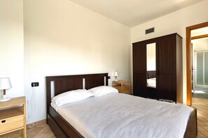 Un dormitorio con cama, mesita de noche, cómoda, espejo y puerta que da a otra habitación.