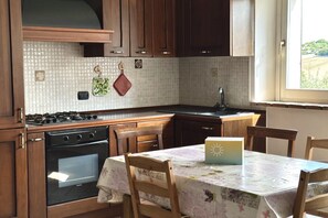 Una cocina con armarios de madera, estufa, horno, lavaplatos y una mesa de comedor con sillas.