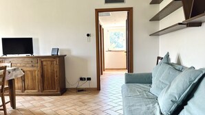 Una sala de estar con sofá, televisión sobre un mueble de madera y un comedor con mesa y sillas.