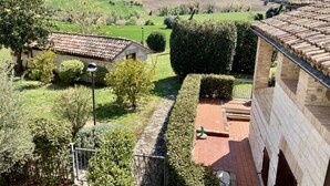 Paisaje rural con un edificio de piedra, un camino pavimentado y un seto.