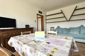 Une chambre avec un lit, une télévision, une table recouverte d’une nappe à motifs floraux et une étagère fixée au mur.