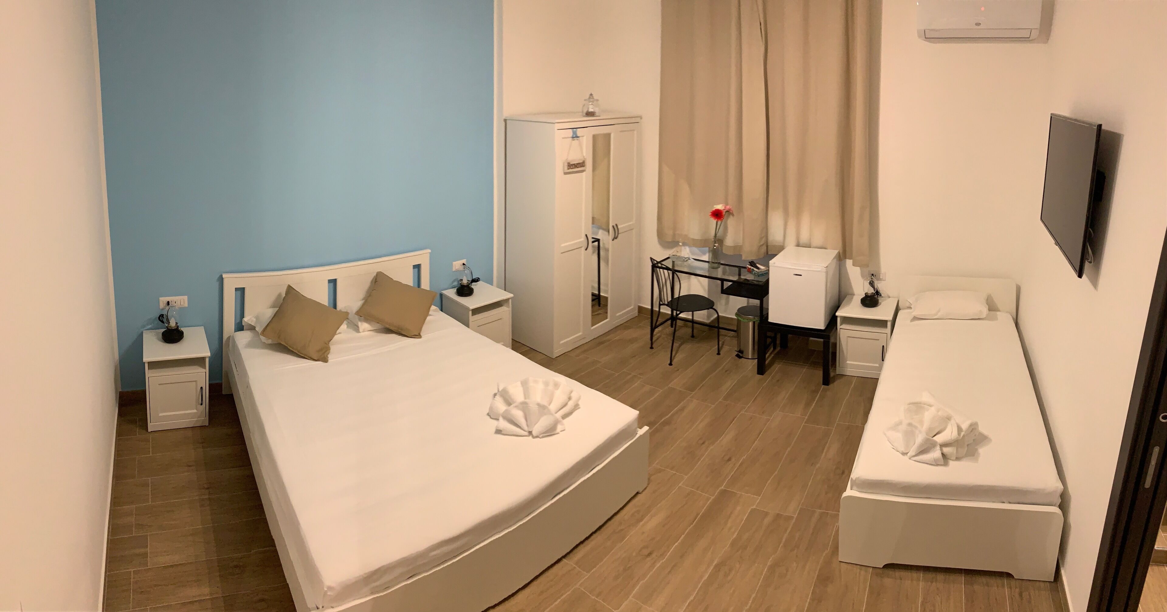 A hotel room with a large bed, a desk, a chair, a wardrobe, and a TV.