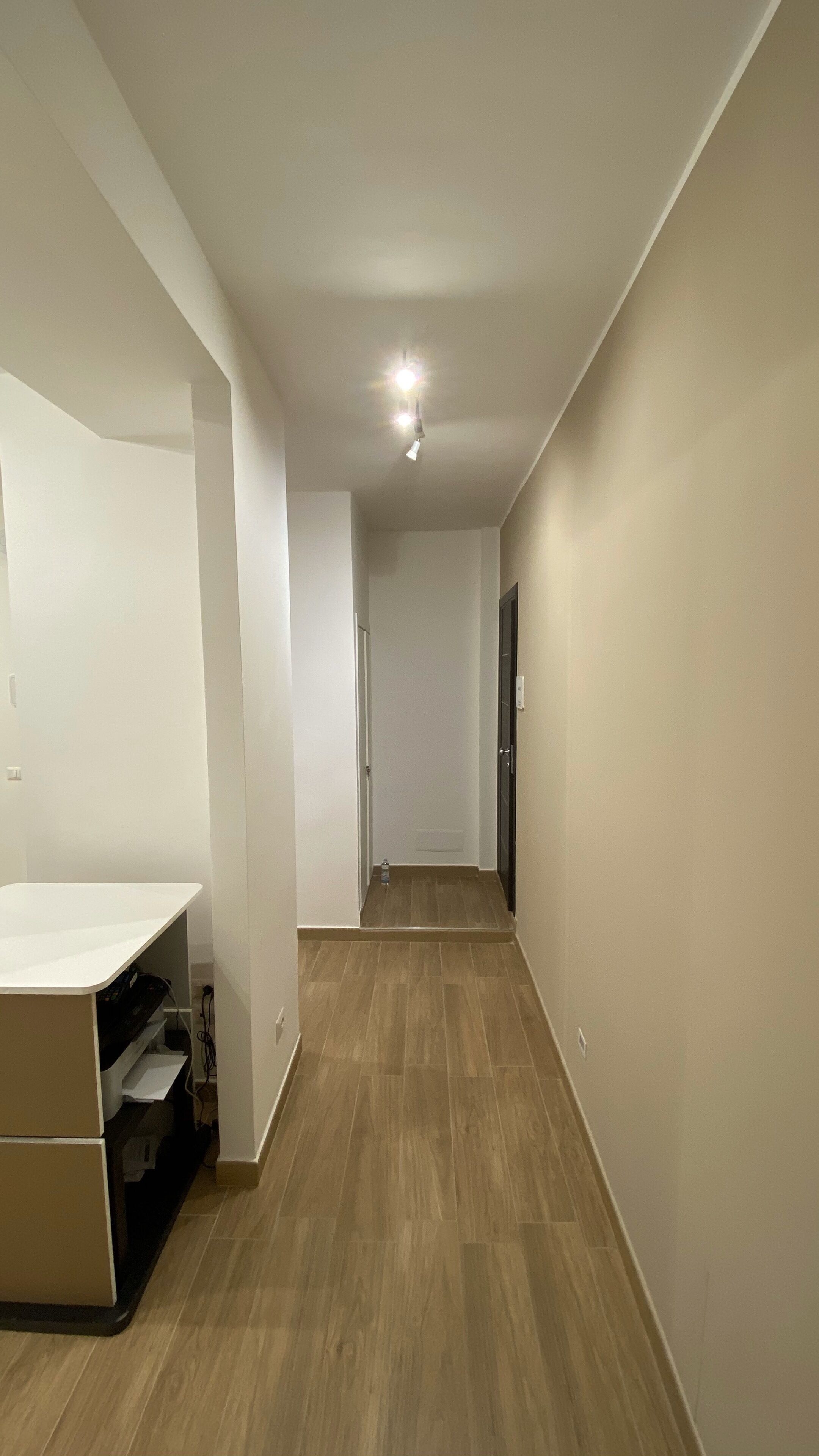 A hallway with wooden flooring, white walls, and a ceiling light.