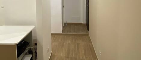 A hallway with wooden flooring, white walls, and a ceiling light.