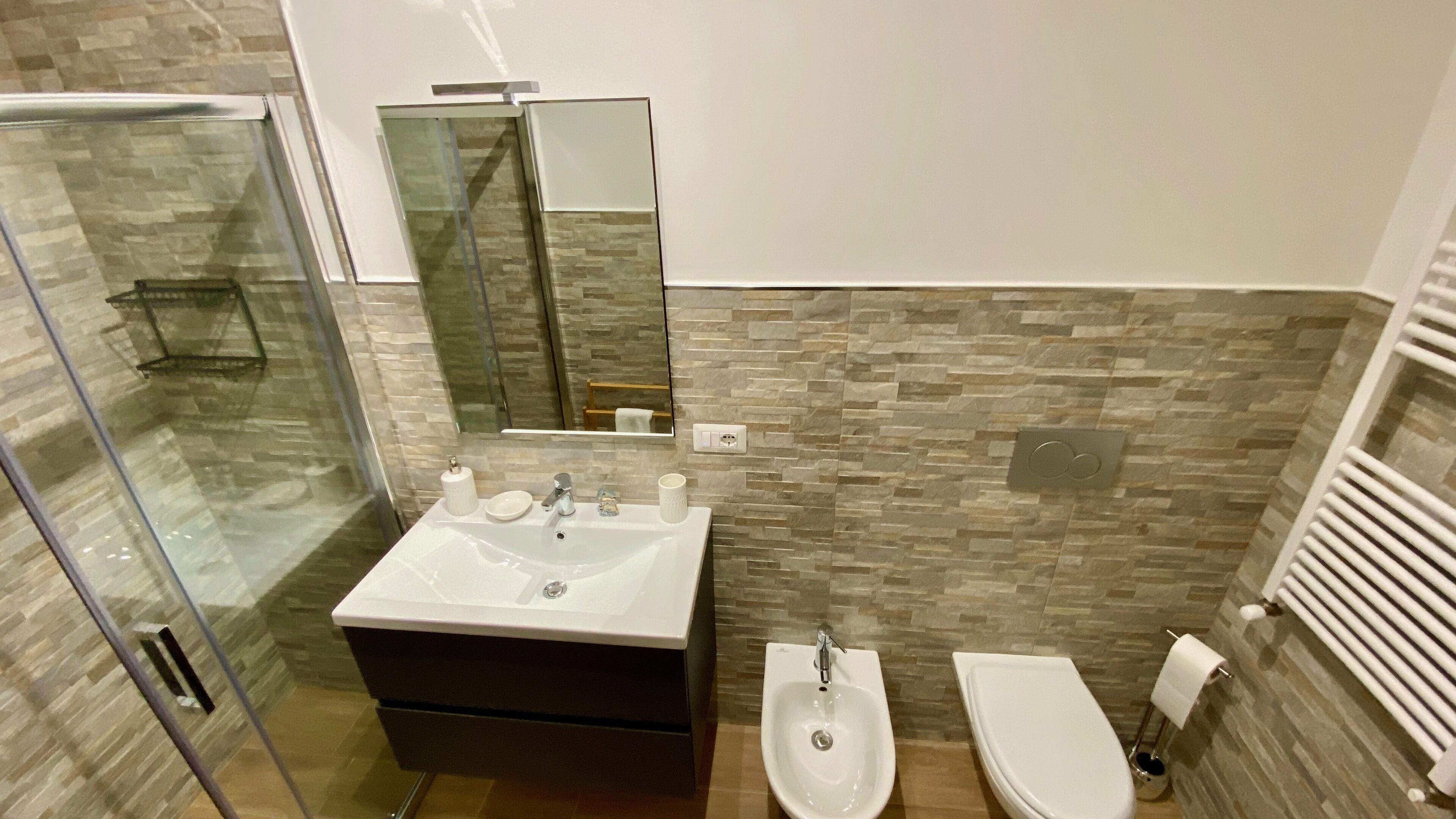 Une salle de bain moderne avec une douche à parois de verre, un meuble-lavabo avec un évier et un miroir, un bidet et des toilettes.