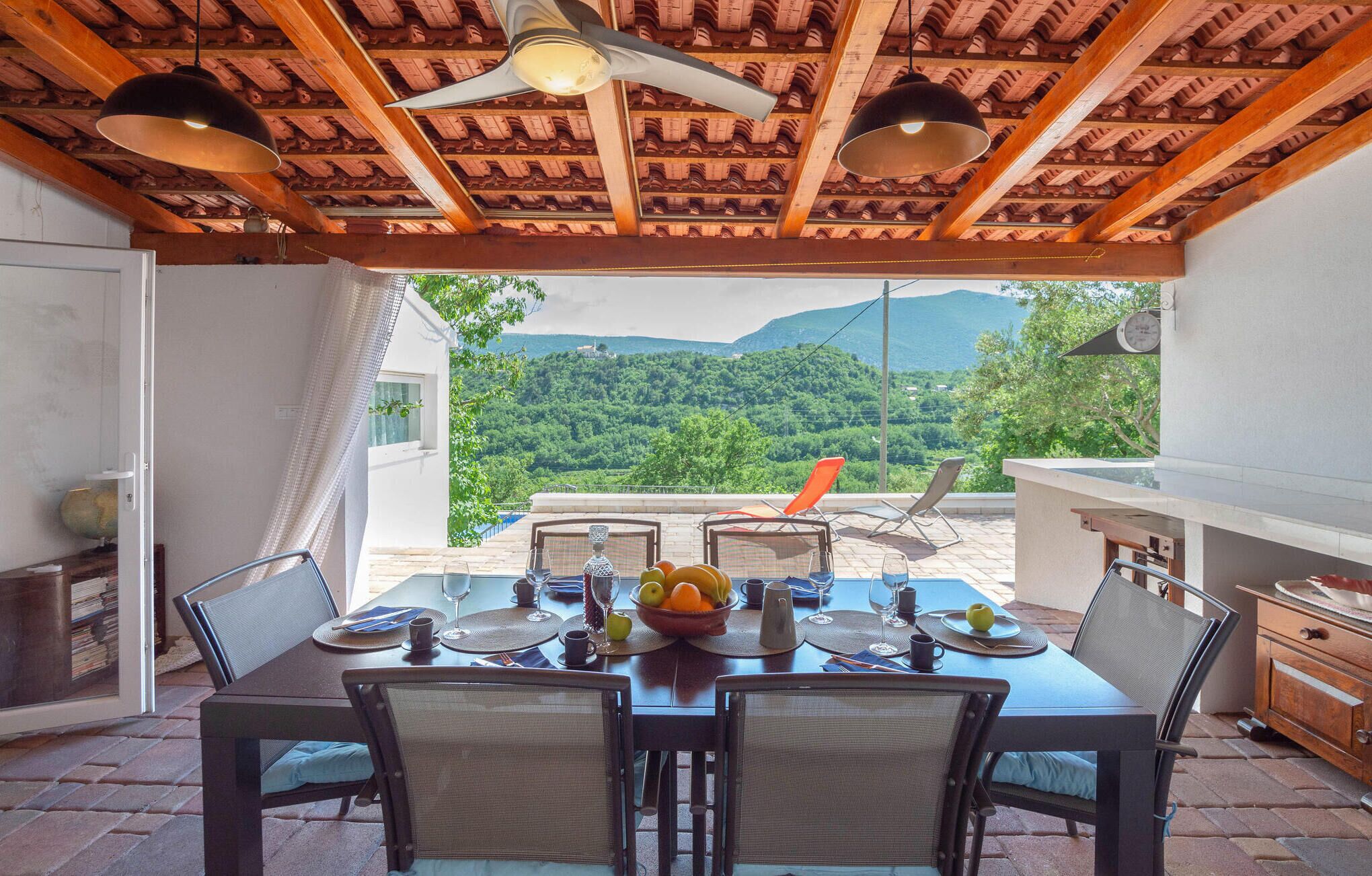 A dining area with a table set for four, a ceiling fan, and a view of a mountainous landscape.
