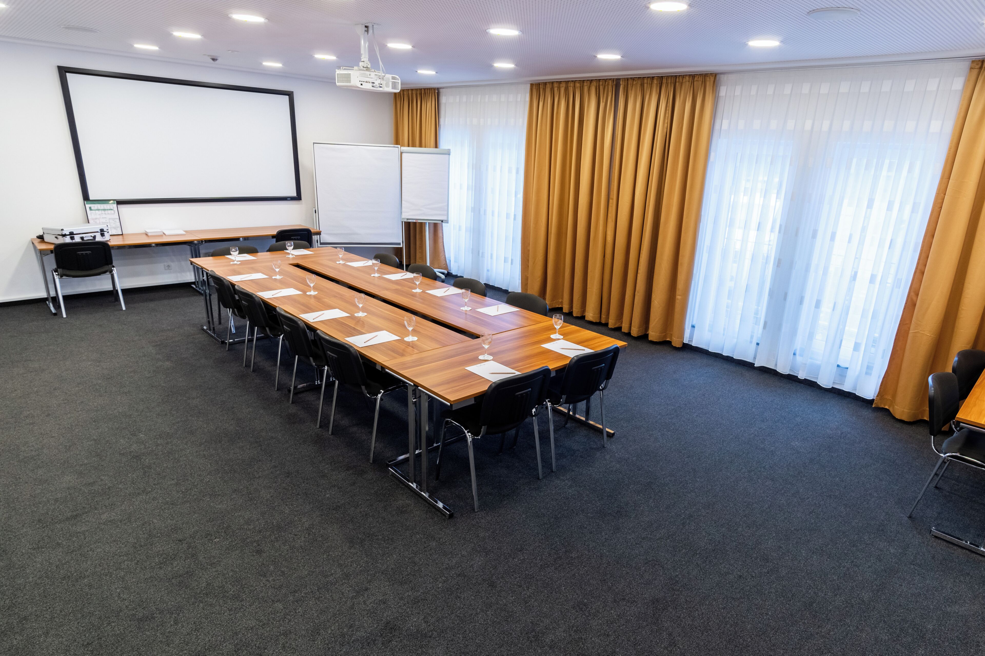 Ein Konferenzraum mit langem Tisch, Stühlen, einem Projektor und einer Whiteboard-Leinwand.