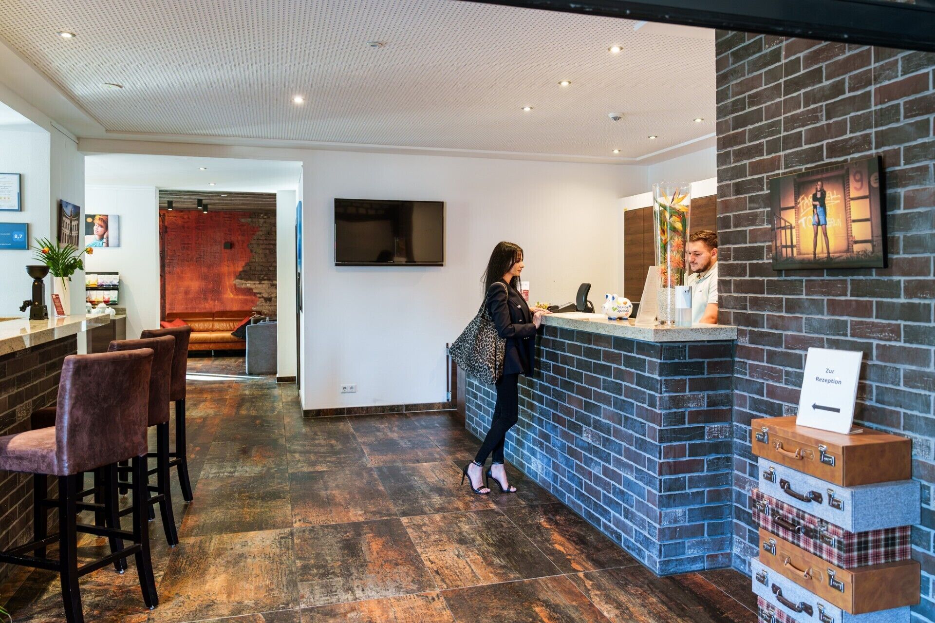Un espace d’accueil d’hôtel avec un mur en briques, un comptoir et un coin salon avec des chaises.
