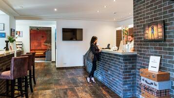 A hotel reception area with a brick wall, a counter, and a seating area with chairs.