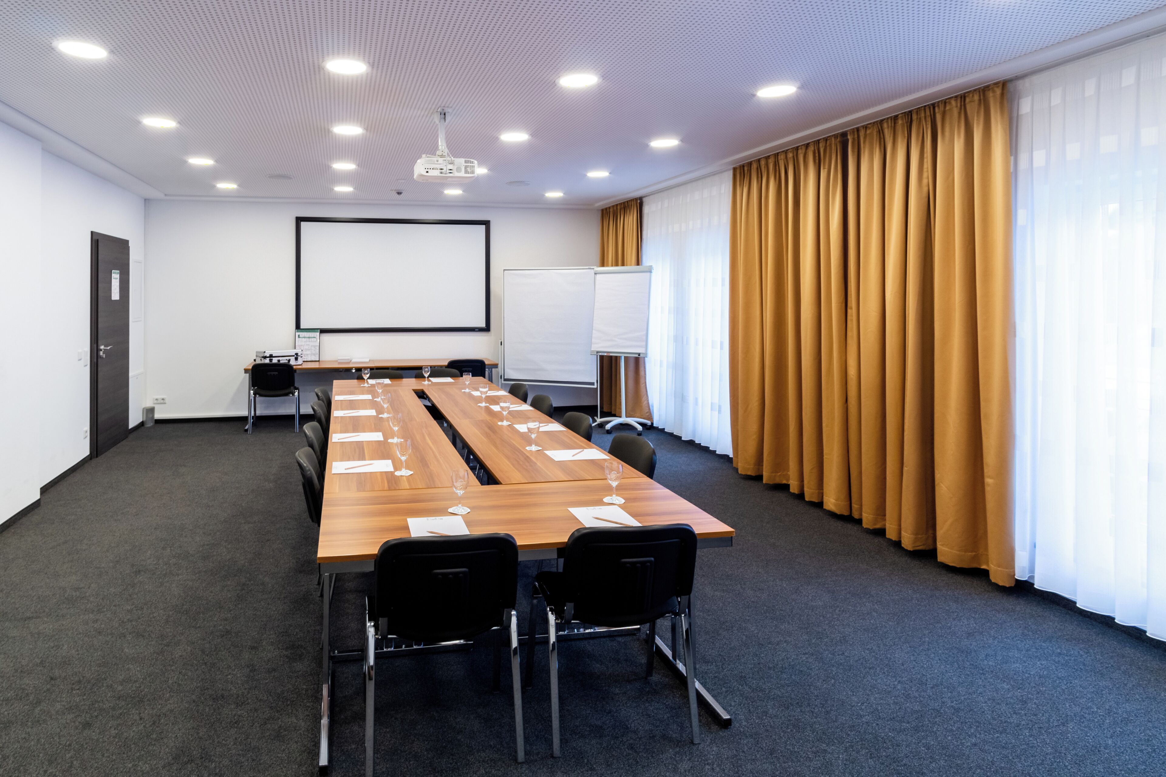 Une salle de conférence équipée d’une longue table, de chaises, d’un écran de projection et d’un tableau blanc.