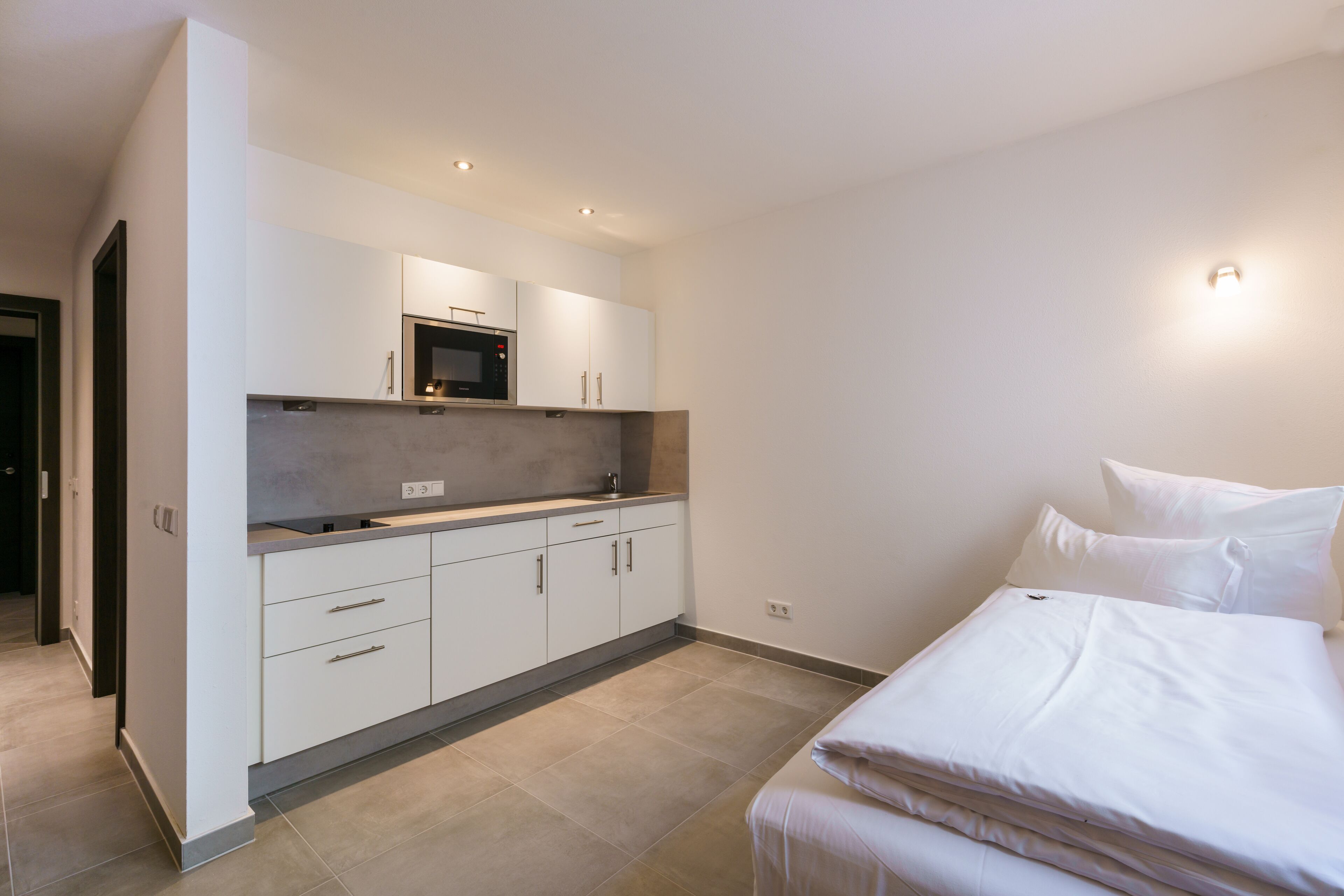 A modern bedroom with a neatly made bed, a built-in wardrobe, and a kitchenette area.