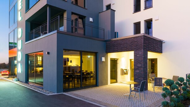 A modern hotel with a glass facade, outdoor seating area, and a visible restaurant inside. - DuDa Boarding Apartments (Reichertshofen)