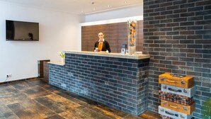 A reception desk with a modern design, a flat-screen TV mounted on the wall, and a brick-patterned wall to the right. - DuDa Boarding Apartments (Reichertshofen)