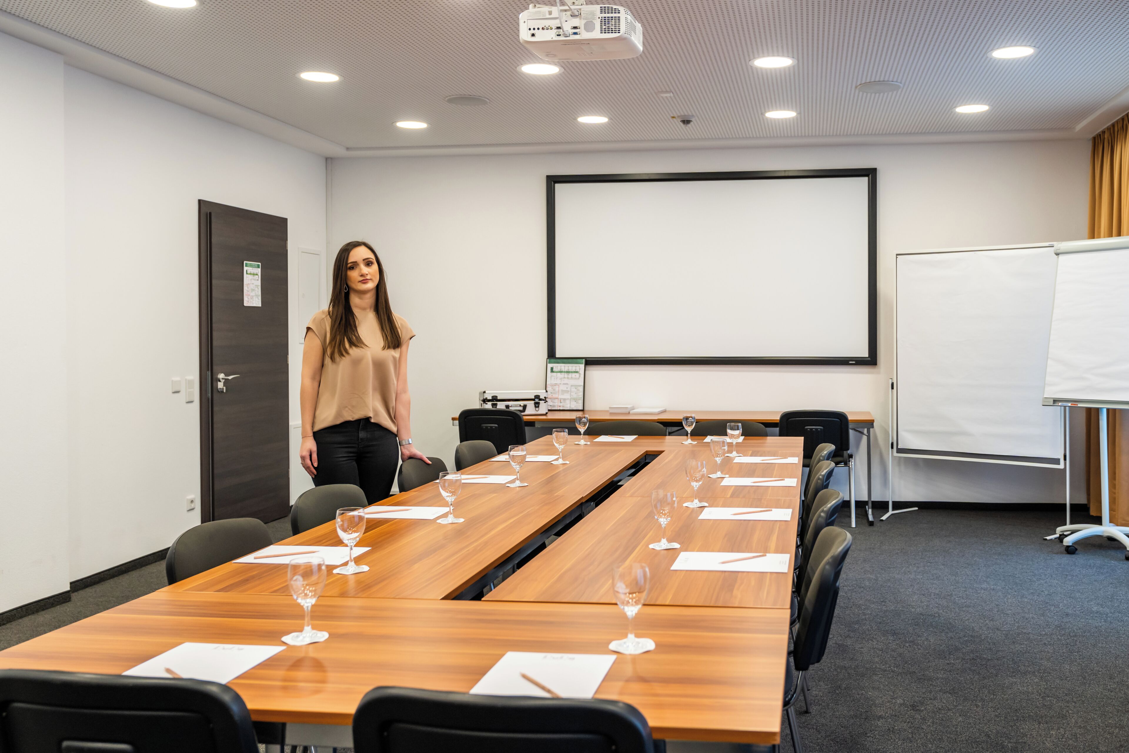 Een vergaderruimte met een lange tafel, stoelen, een projectiescherm en een whiteboard.