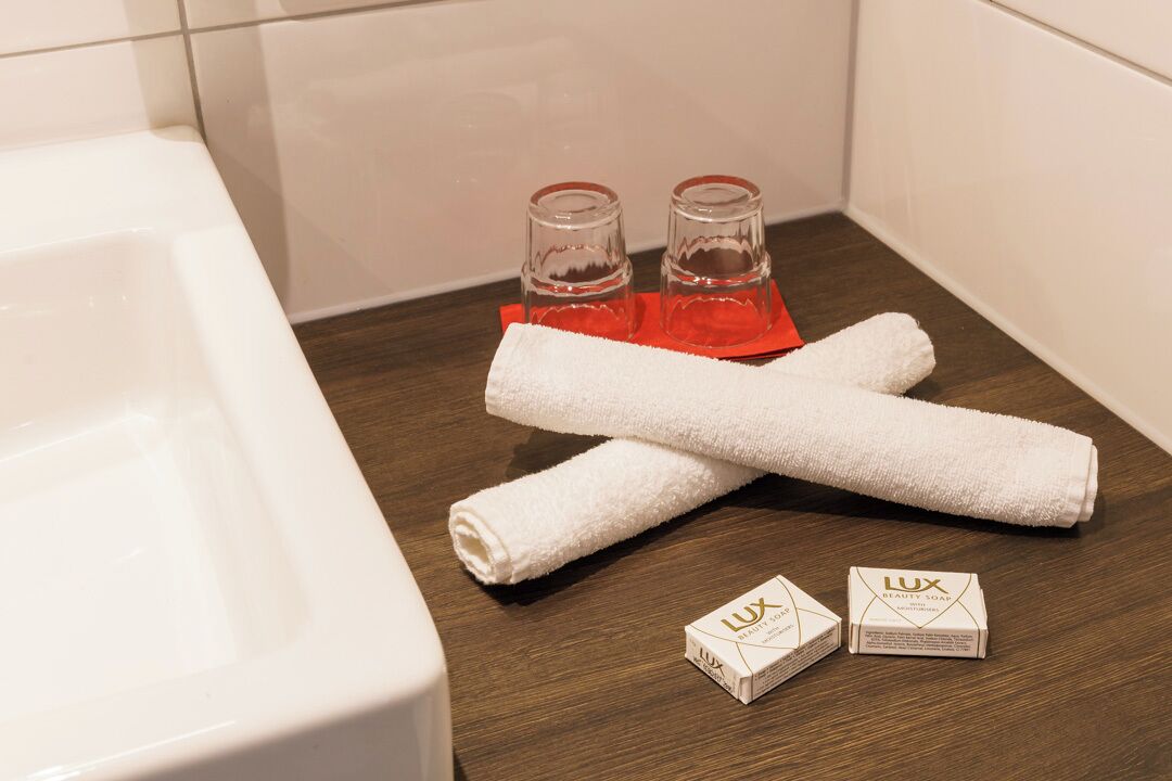 Un baño con una bañera blanca, dos botellas de vidrio y dos cajas de Jabón de Belleza Lux sobre un piso de madera.