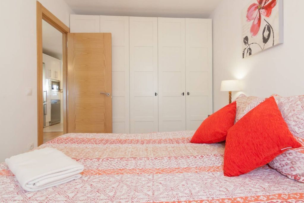 Een slaapkamer met een bed, een houten deur, een witte kledingkast en een schilderij aan de muur.