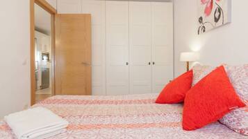 Een slaapkamer met een bed, een houten deur, een witte kledingkast en een schilderij aan de muur.