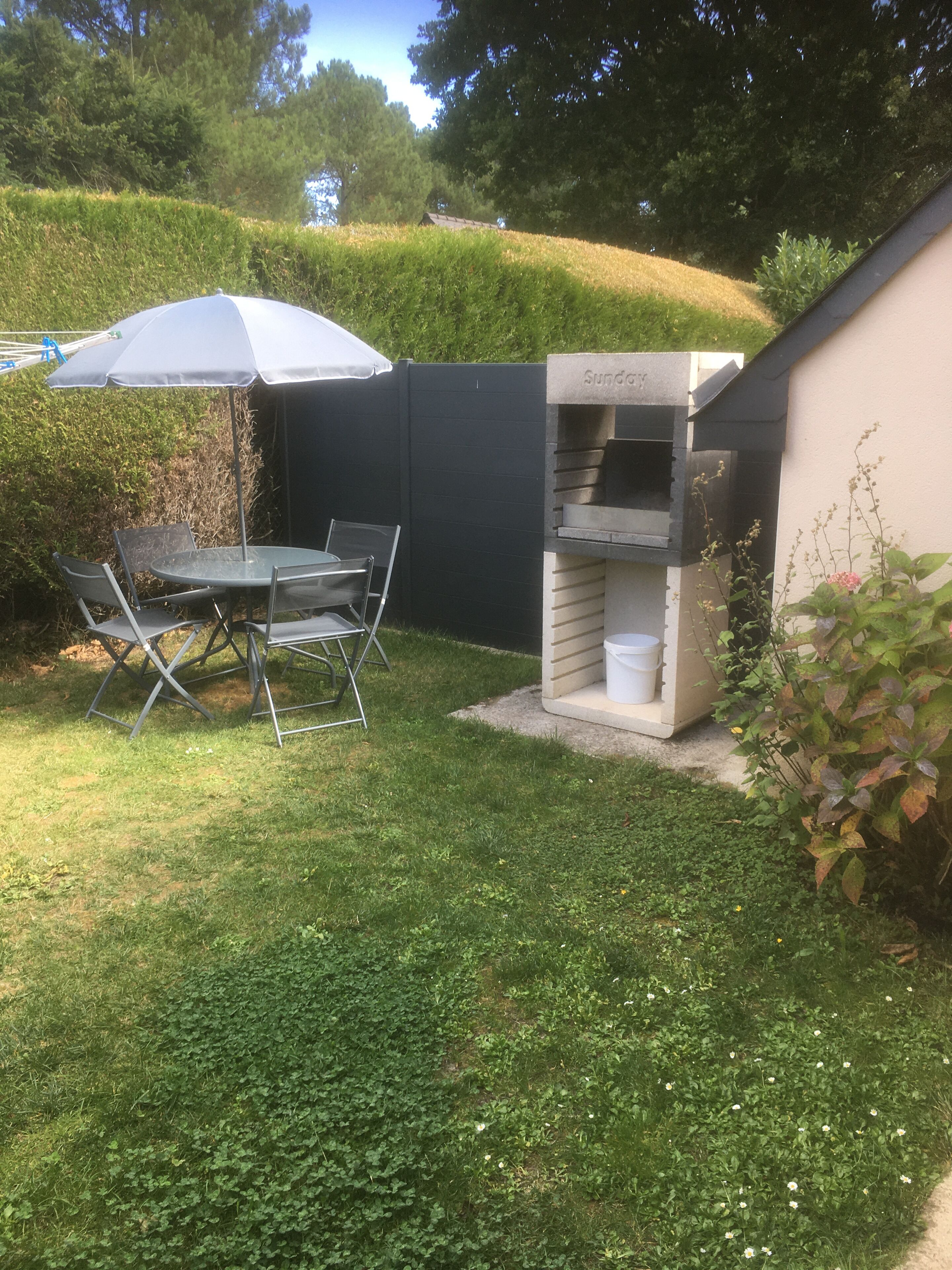 A backyard with a grill, a table with chairs, and a blue umbrella.