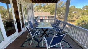 A covered outdoor area with a table and chairs, a patterned rug, and a view of trees and a house in the background. - Stunning 5 Bedroom Home, Short Walk to Beach, Includes 2 Golf Carts, 809 Bonito Road 809 Bonito Drive (Fripp Island)