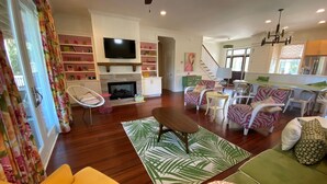 A spacious living room with a fireplace, a television, and a staircase leading to the upper floor. - Stunning 5 Bedroom Home, Short Walk to Beach, Includes 2 Golf Carts, 809 Bonito Road 809 Bonito Drive (Fripp Island)