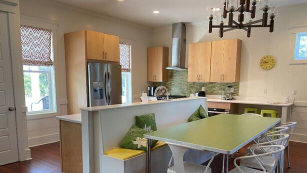 A modern kitchen with wooden cabinets, a stainless steel refrigerator, a built-in island with seating, and a dining area with white chairs. - Stunning 5 Bedroom Home, Short Walk to Beach, Includes 2 Golf Carts, 809 Bonito Road 809 Bonito Drive (Fripp Island)