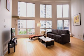 A spacious living room with a large window, a sofa, a coffee table, and a television. - Rare luxury Downtown Vancouver loft/sleeps 8/2 bedroom + 2 bath/1500sf + parking (Vancouver)
